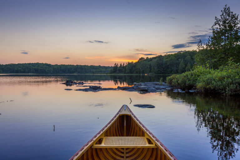 Haliburton attractions: canoe on a lake at sunset surrounded by trees